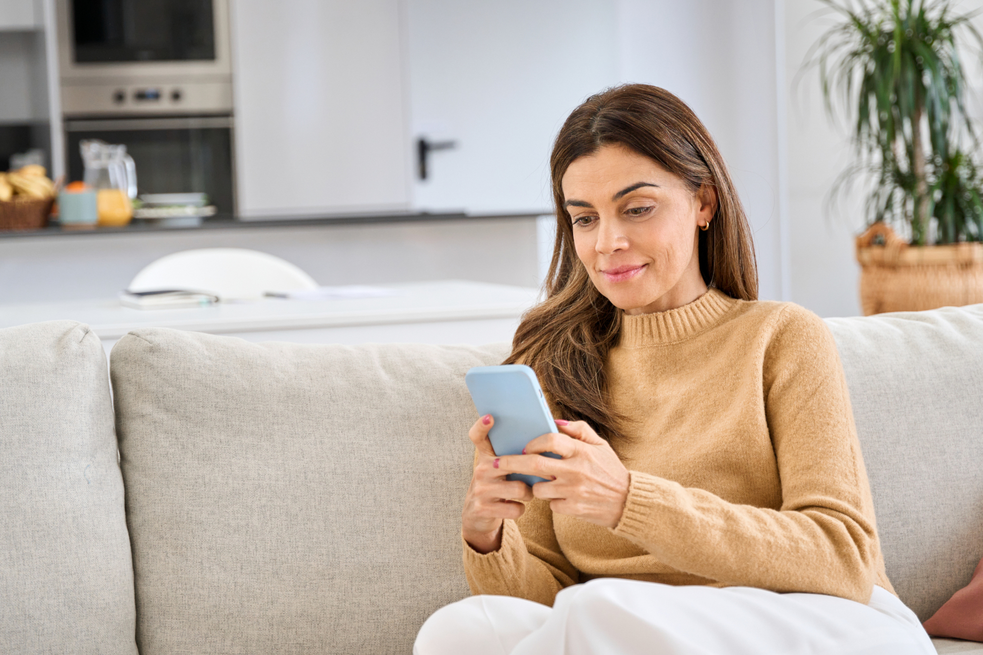 Relaxed middle aged older woman using smartphone sitting on couch at home